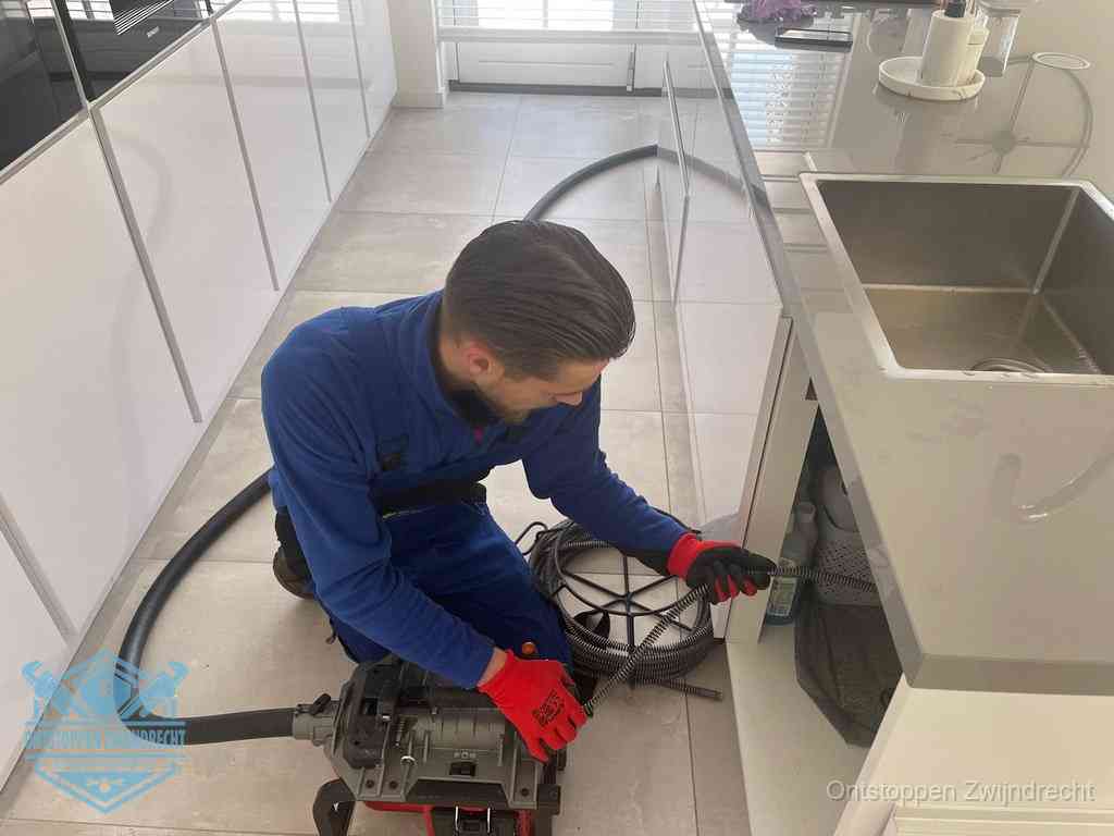 Een monteur ontstopt de keukenafvoer onder de spoelbak met een elektrische veermachine in Zwijndrecht