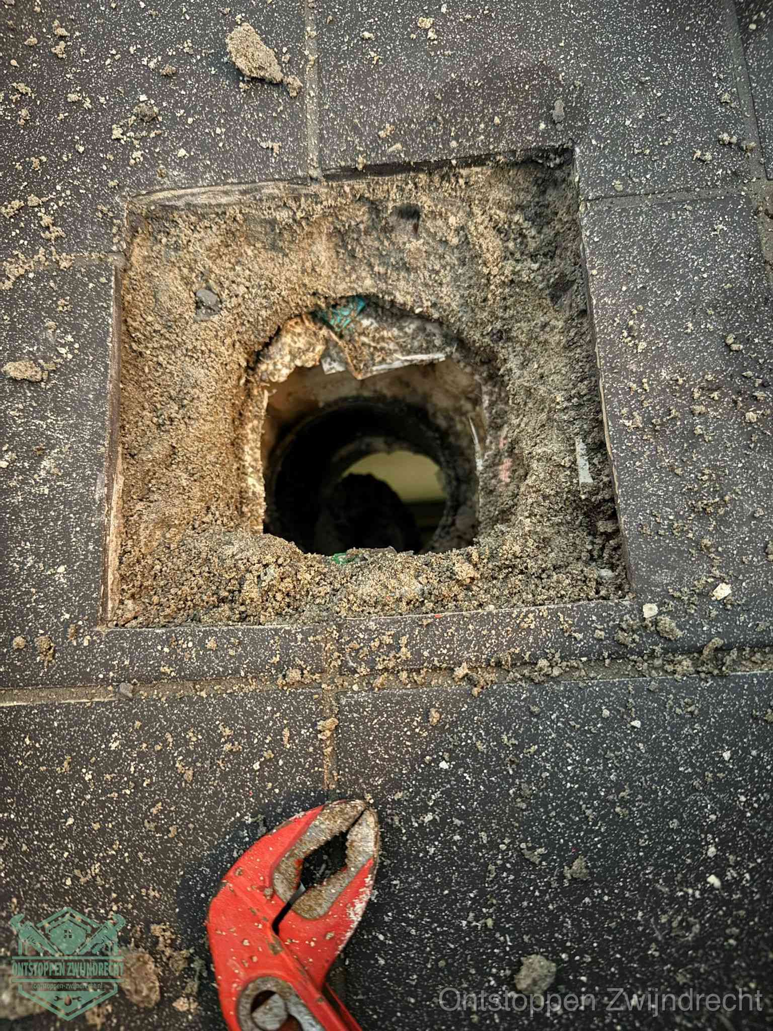 Een geopend rioolputje in een betontegelvloer met losgemaakt rooster en een zichtbare ronde afvoerbuis, het achterhalen waar de afvoerverstopping zit in Zwijndrecht