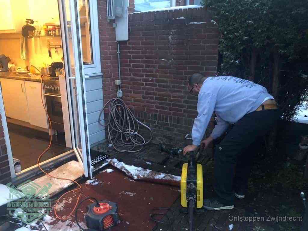 Een monteur werkt buiten bij een open riool-/grondput met een elektrische ontstoppingsmachine om een verborgen afvoerprobleem op te sporen in Zwijndrecht