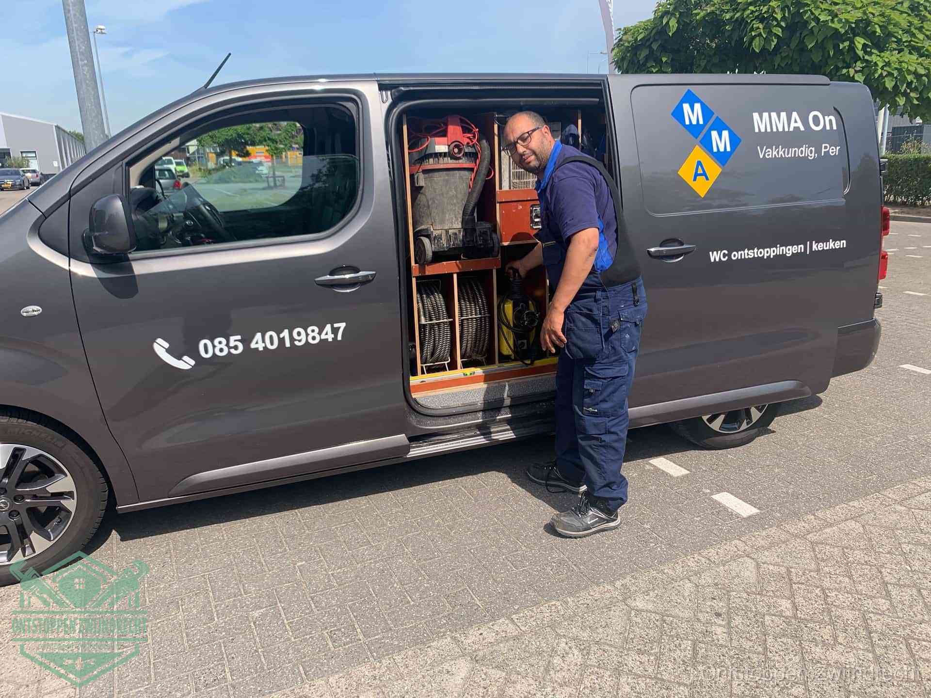 Een monteur bij de open schuifdeur van zijn bedrijfsbus op een parkeerplaats, klaar om de oorzaak van terugkerende afvoerverstoppingen aan te pakken in Zwijndrecht